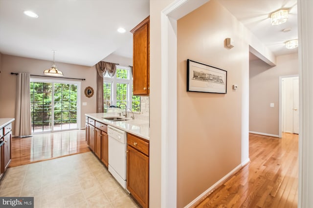 kitchen with brown cabinetry, baseboards, light countertops, a sink, and dishwasher