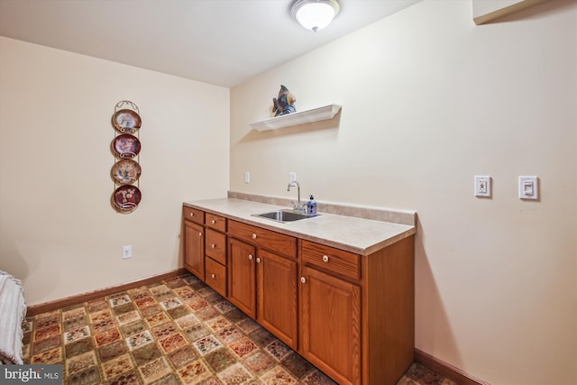 kitchen with open shelves, brown cabinets, a sink, light countertops, and baseboards