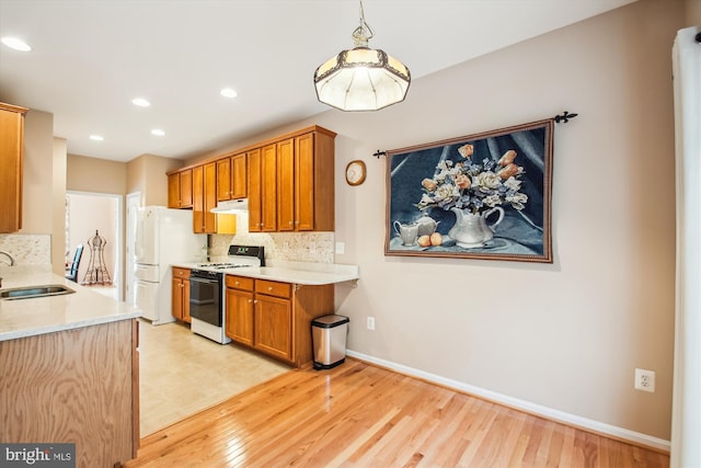 kitchen with a sink, range with gas stovetop, freestanding refrigerator, tasteful backsplash, and under cabinet range hood