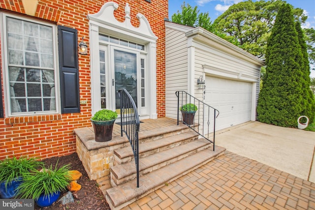 doorway to property featuring an attached garage, driveway, and brick siding
