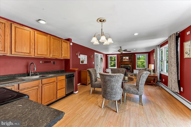 kitchen featuring dark countertops, a fireplace, dishwasher, a sink, and light wood-style flooring