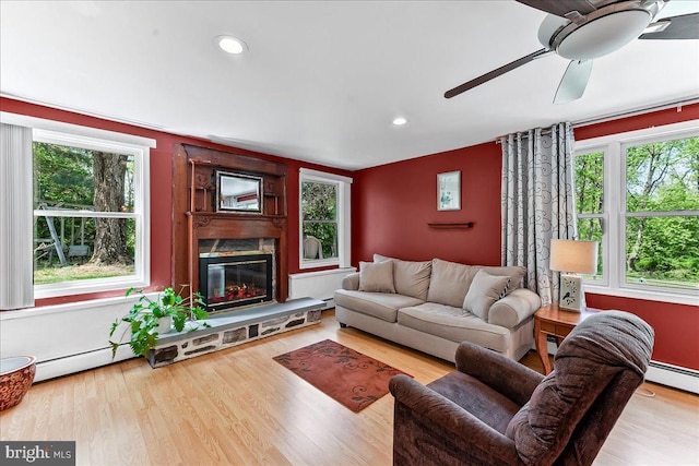 living room with a glass covered fireplace, wood finished floors, ceiling fan, baseboard heating, and recessed lighting