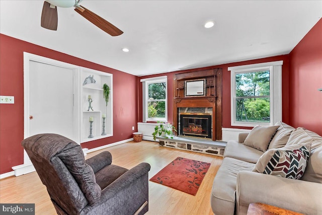 living room featuring a glass covered fireplace, ceiling fan, and wood finished floors