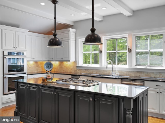kitchen featuring appliances with stainless steel finishes, a sink, dark cabinetry, a kitchen island, and beamed ceiling