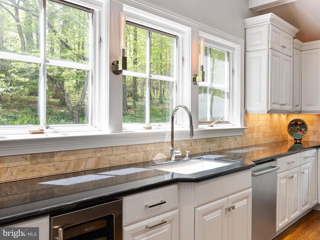 kitchen with decorative backsplash, wine cooler, dark countertops, white cabinets, and a sink