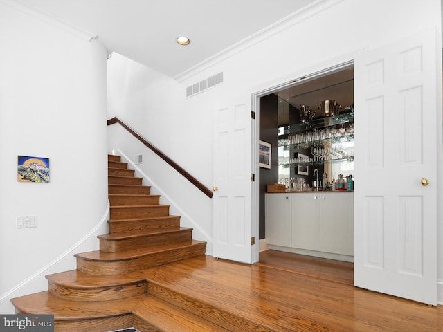 stairway with crown molding, recessed lighting, wood finished floors, visible vents, and a bar