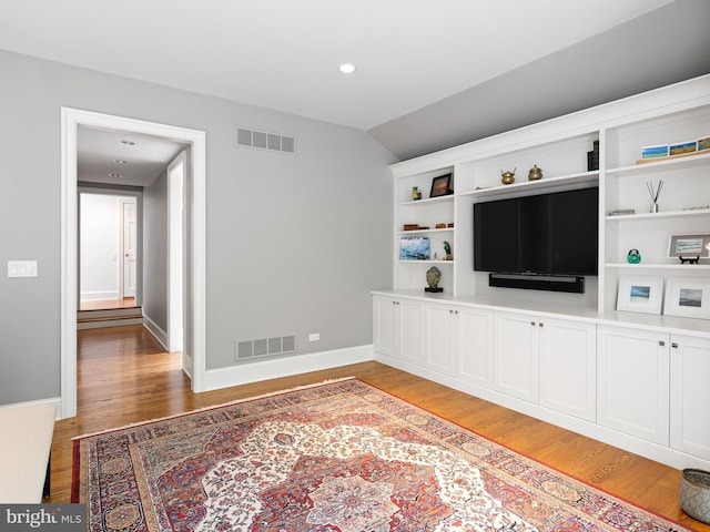 living area with light wood-style floors, baseboards, vaulted ceiling, and visible vents