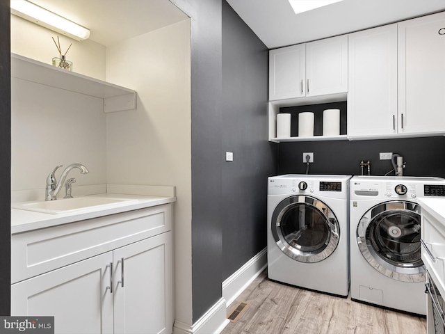 laundry area featuring independent washer and dryer, cabinet space, a sink, light wood finished floors, and baseboards