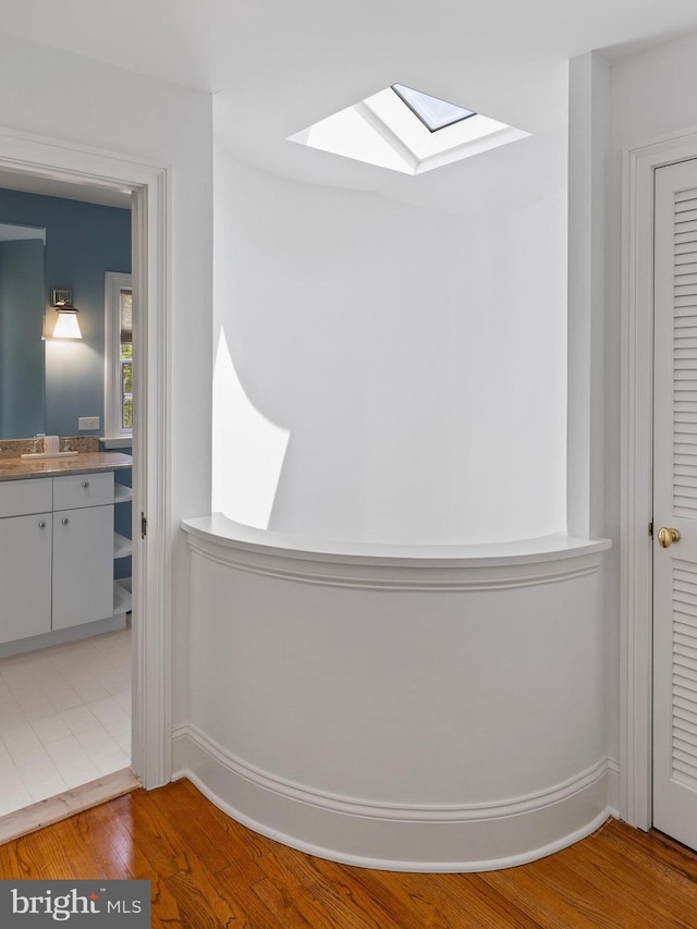 room details with baseboards, a sink, wood finished floors, and a skylight