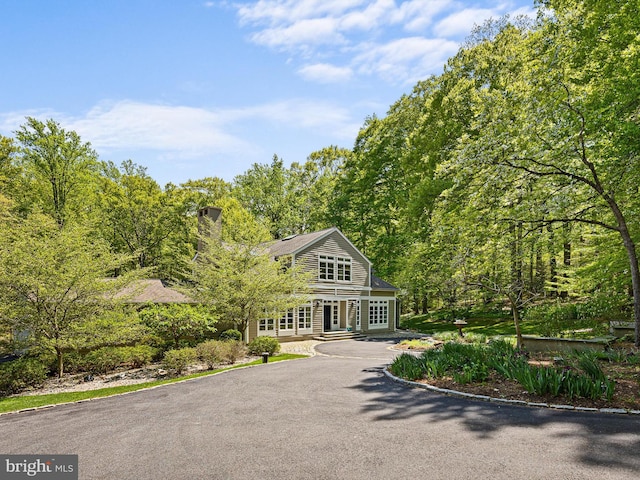 view of front of property featuring a view of trees, driveway, french doors, and a chimney