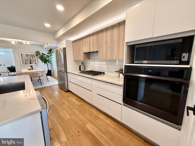 kitchen featuring light wood-style floors, modern cabinets, white cabinetry, appliances with stainless steel finishes, and backsplash