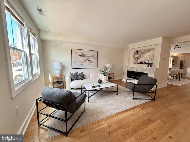 living room with a high end fireplace, baseboards, light wood-style flooring, and visible vents