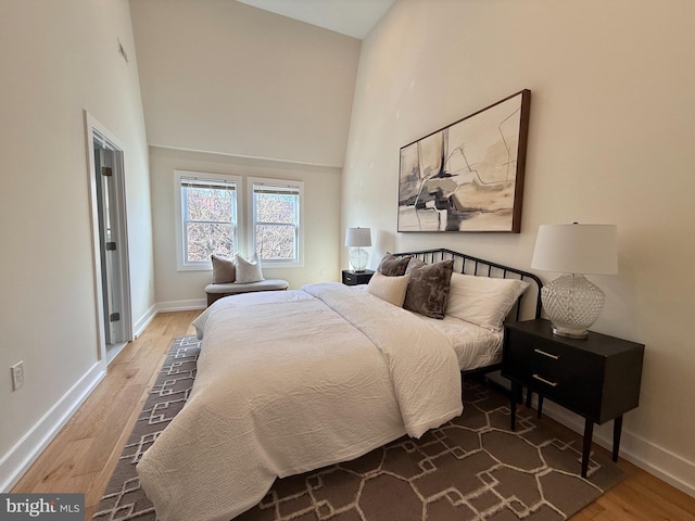 bedroom featuring baseboards, wood finished floors, and a towering ceiling