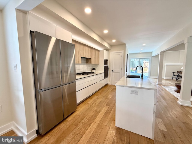 kitchen with appliances with stainless steel finishes, a sink, light wood finished floors, white cabinetry, and modern cabinets