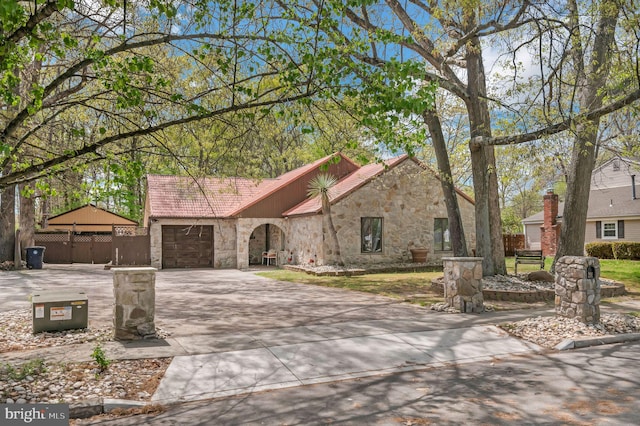 view of front facade with fence, driveway, stone siding, and a garage