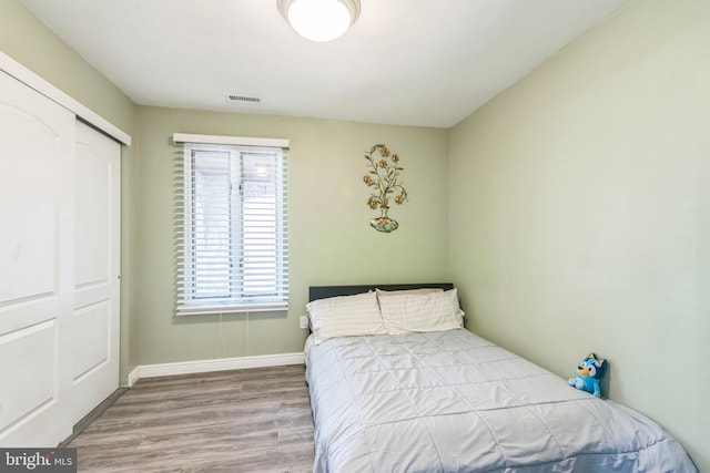 bedroom with baseboards, a closet, wood finished floors, and visible vents