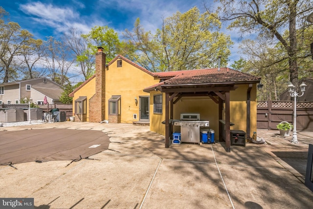 back of property with a tiled roof, a chimney, a patio area, fence, and stucco siding