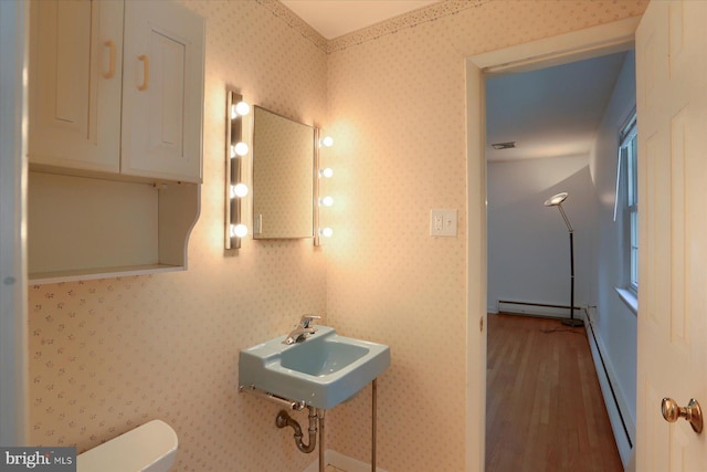 bathroom with a sink, baseboard heating, toilet, wood finished floors, and visible vents