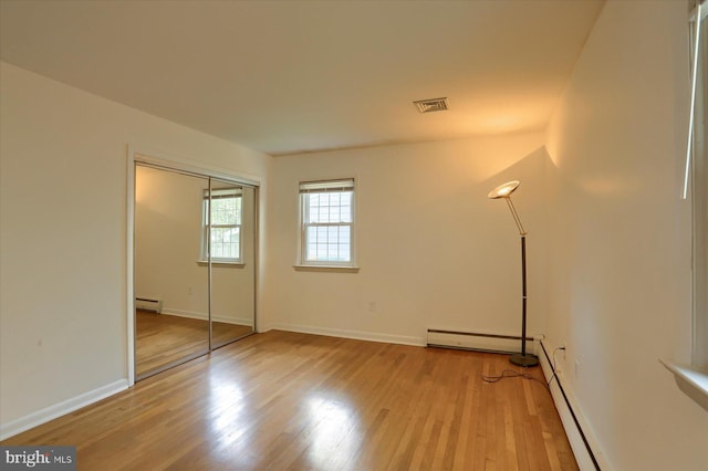 unfurnished bedroom featuring visible vents, a baseboard heating unit, baseboards, and wood finished floors
