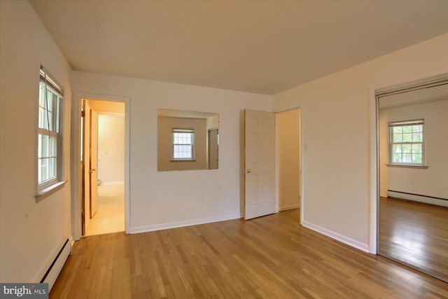 unfurnished bedroom featuring baseboards, baseboard heating, light wood finished floors, and ensuite bath
