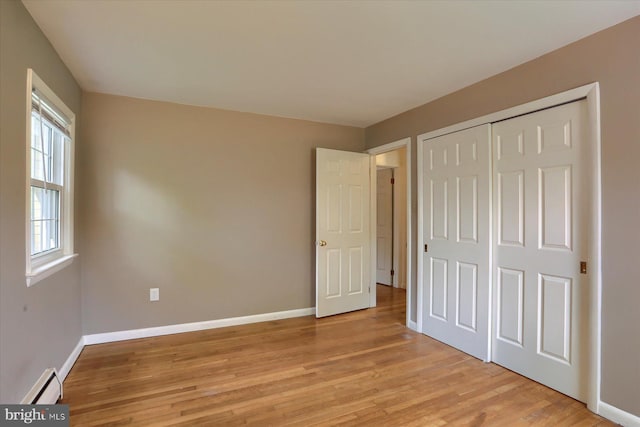 unfurnished bedroom with baseboards, a baseboard radiator, a closet, and light wood-type flooring