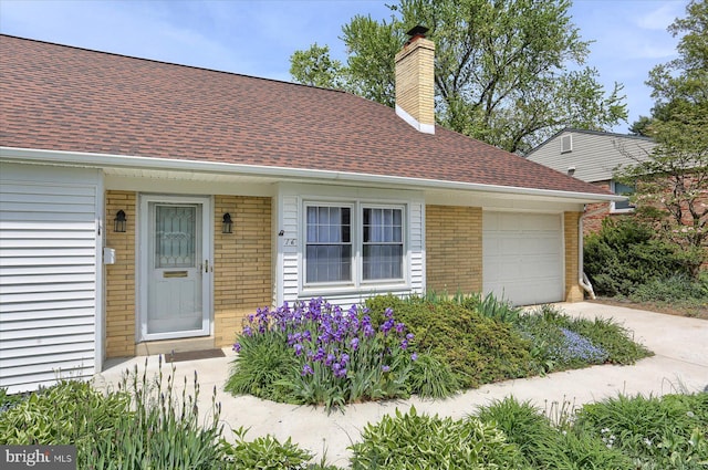 view of front of house featuring roof with shingles, an attached garage, brick siding, a chimney, and concrete driveway