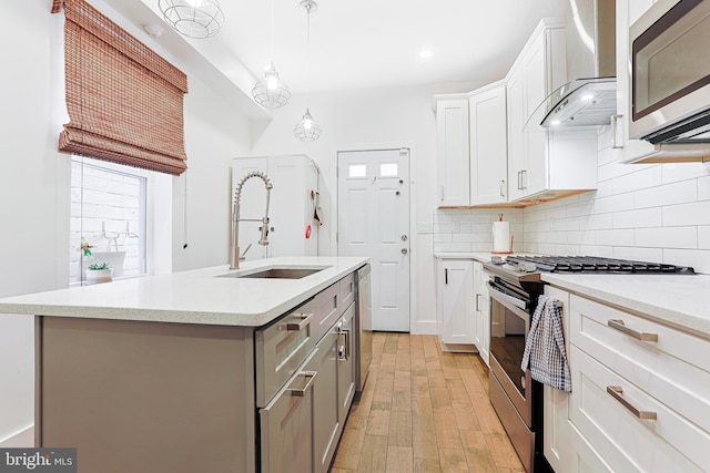 2325 W Thompson St, Philadelphia, PA 19121 - kitchen featuring a center island with sink, light wood-type flooring, a sink, stainless steel appliances, and wall chimney exhaust hood