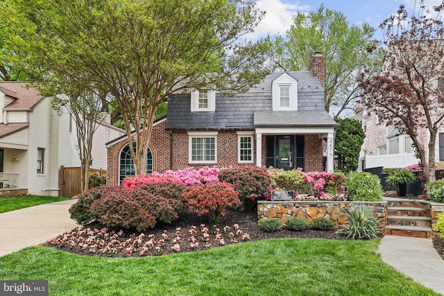 new england style home with fence, a high end roof, brick siding, a front yard, and a chimney