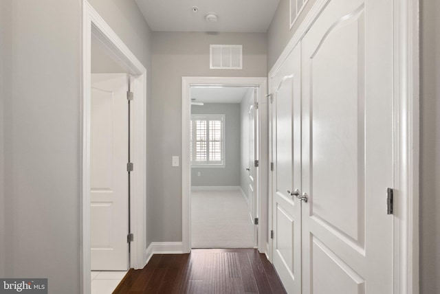 hallway featuring visible vents, baseboards, and dark wood-type flooring