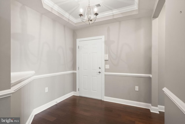 entrance foyer featuring wood finished floors, a raised ceiling, baseboards, a notable chandelier, and ornamental molding