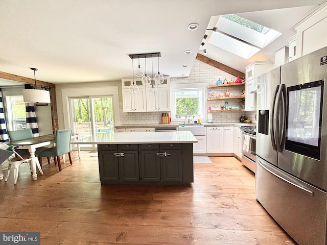 kitchen featuring appliances with stainless steel finishes, white cabinets, a skylight, light countertops, and backsplash