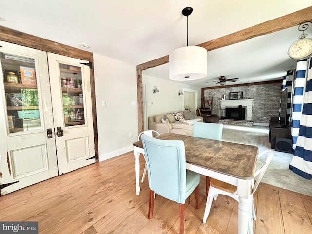 dining space with light wood-style floors, ceiling fan, a fireplace with raised hearth, and baseboards