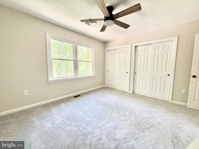 unfurnished bedroom featuring two closets, baseboards, and carpet floors