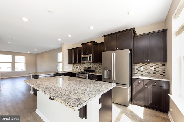 kitchen featuring light wood-style flooring, appliances with stainless steel finishes, dark brown cabinetry, and tasteful backsplash