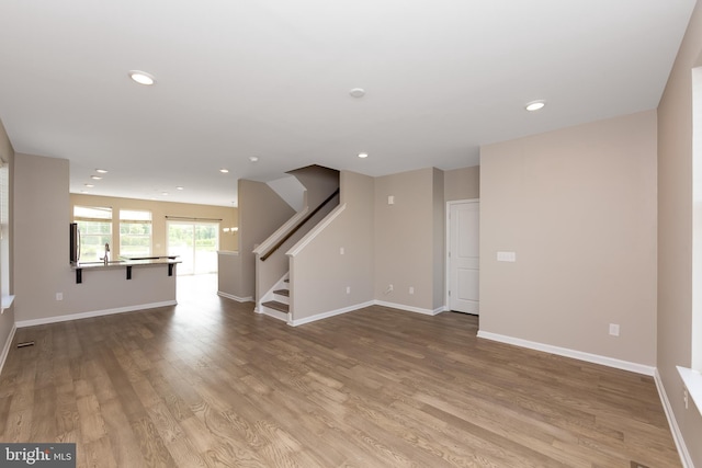 unfurnished living room with recessed lighting, baseboards, stairs, and wood finished floors