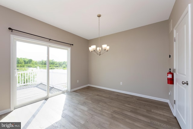 empty room featuring baseboards, an inviting chandelier, wood finished floors, and visible vents