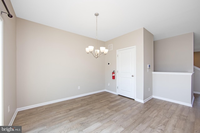 unfurnished room with baseboards, visible vents, wood finished floors, and a chandelier