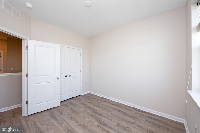 unfurnished bedroom with baseboards, a closet, wood finished floors, and visible vents
