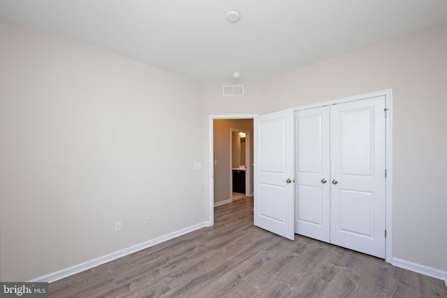 unfurnished bedroom with baseboards, a closet, wood finished floors, and visible vents