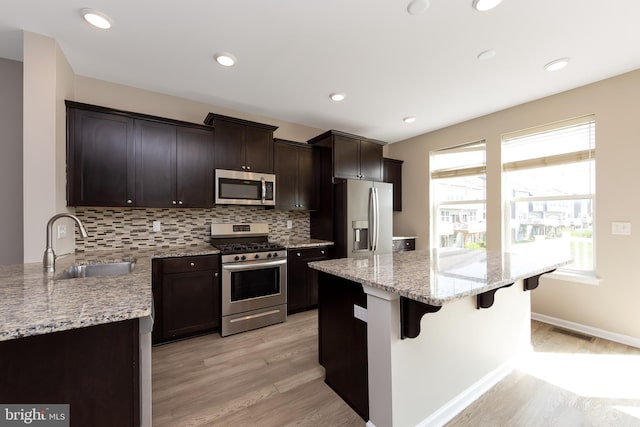 kitchen with a kitchen breakfast bar, backsplash, appliances with stainless steel finishes, a sink, and light wood-style floors