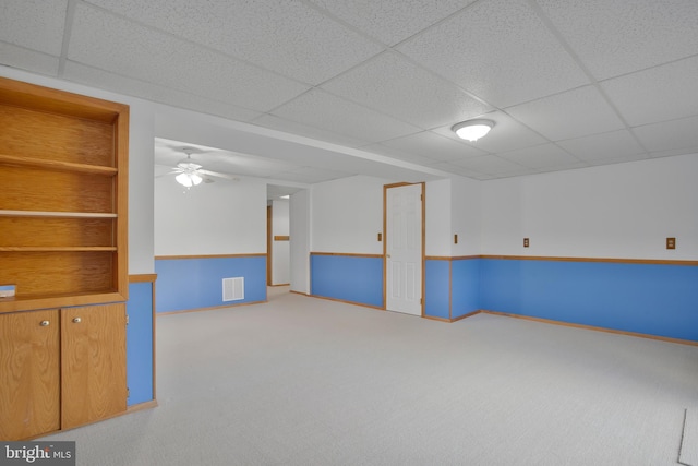 basement featuring a ceiling fan, a paneled ceiling, visible vents, carpet floors, and baseboards