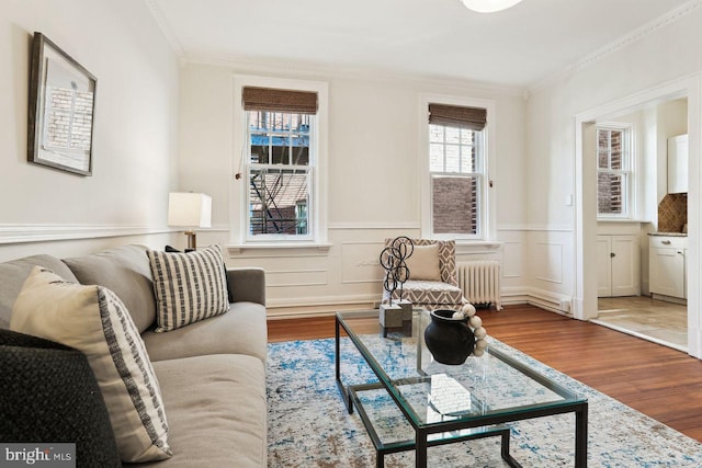 living area featuring radiator, ornamental molding, a wainscoted wall, and wood finished floors