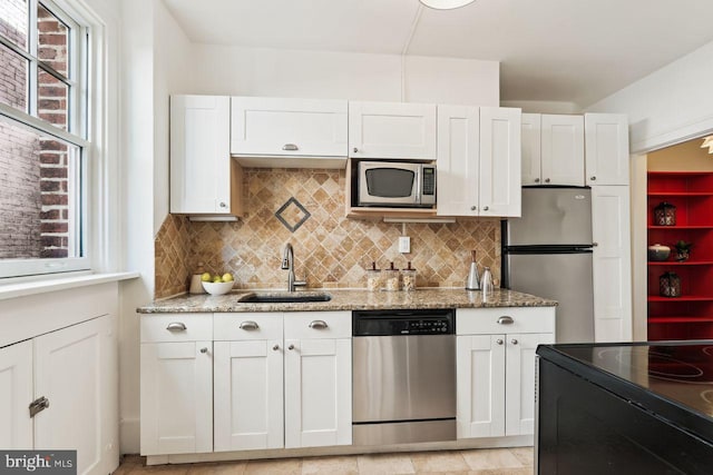 kitchen featuring tasteful backsplash, light stone countertops, a sink, stainless steel appliances, and white cabinetry