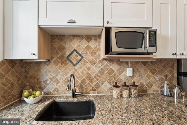 kitchen featuring backsplash, a sink, white cabinets, stainless steel microwave, and dark stone counters