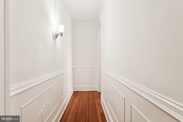 corridor with a wainscoted wall, ornamental molding, a decorative wall, and dark wood-style flooring