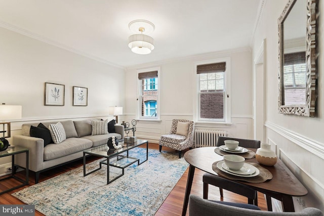 living area with crown molding, wood finished floors, radiator, and a wainscoted wall
