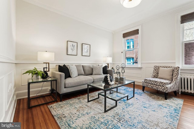 living room with wainscoting, a decorative wall, radiator heating unit, wood finished floors, and ornamental molding
