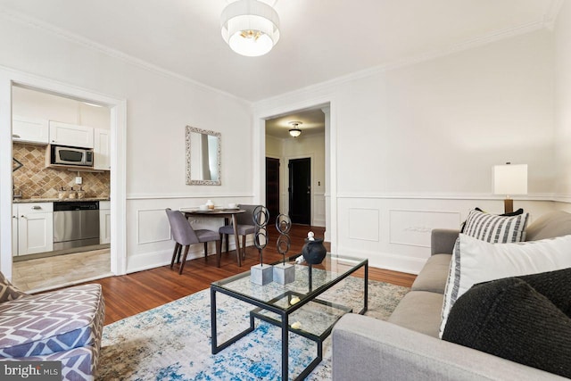 living area featuring ornamental molding, light wood finished floors, and a wainscoted wall