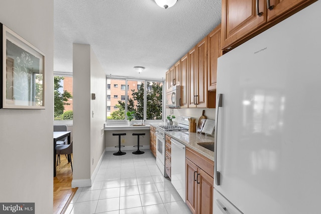 1301 S Arlington Ridge Rd Unit 208, Arlington, VA 22202 - kitchen featuring stainless steel appliances, baseboards, brown cabinetry, a textured ceiling, and light stone countertops