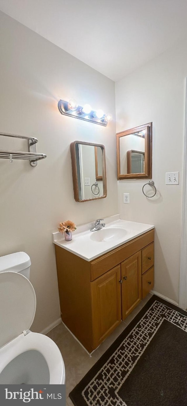 half bath with toilet, baseboards, and vanity